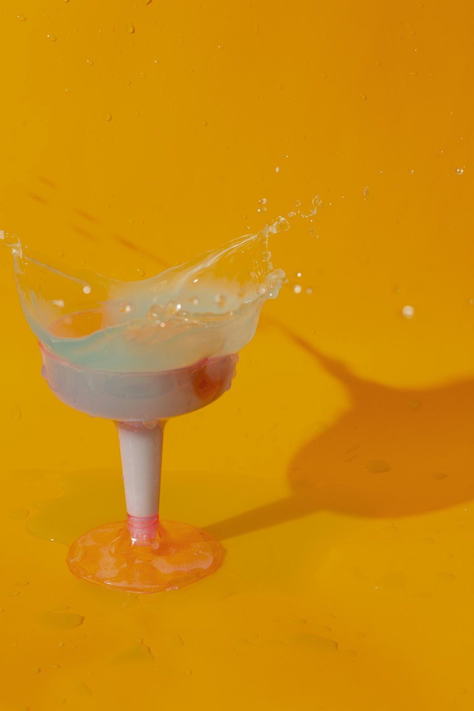 Cocktail glass with a splash of liquid on a yellow background