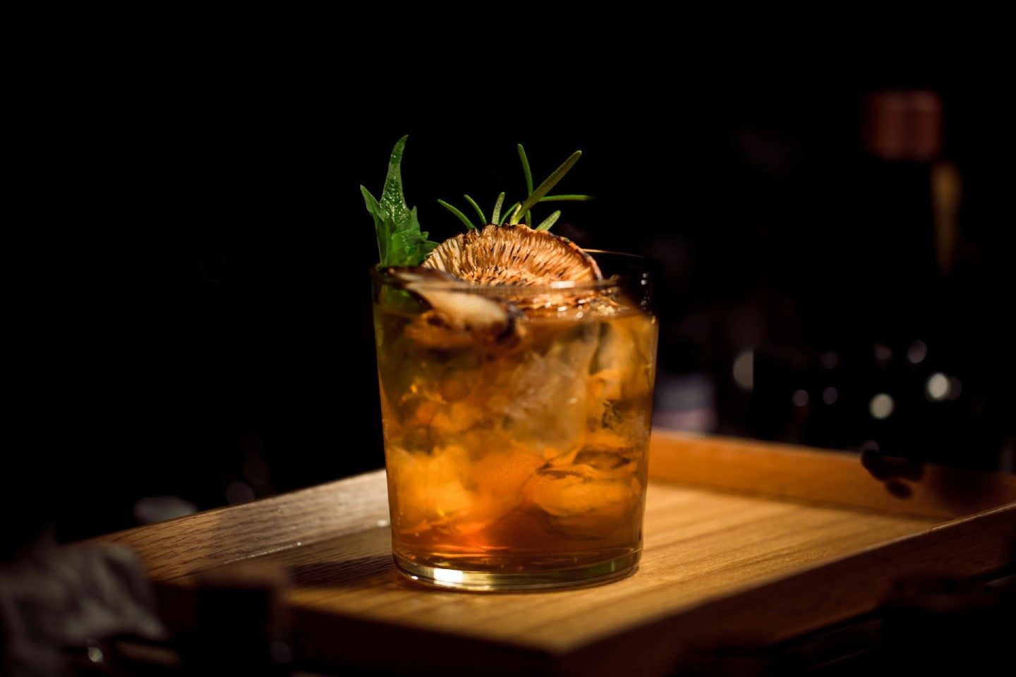 Rum cocktail garnished with fruit and herbs, on a wooden platter.
